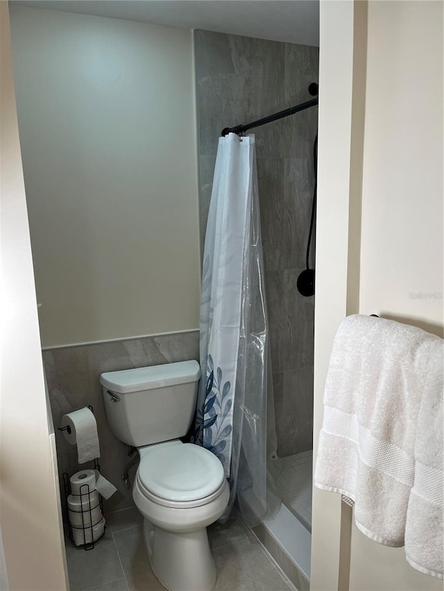 full bath with a stall shower, wainscoting, toilet, tile patterned flooring, and tile walls