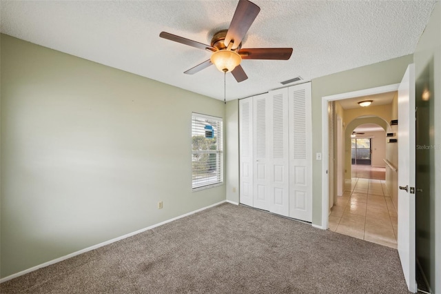 unfurnished bedroom with ceiling fan, light colored carpet, a closet, and a textured ceiling