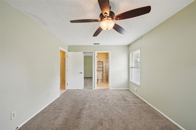 unfurnished bedroom featuring ceiling fan, carpet floors, a textured ceiling, and ensuite bath