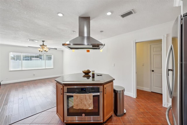 kitchen with appliances with stainless steel finishes, island range hood, light tile patterned floors, ceiling fan, and crown molding