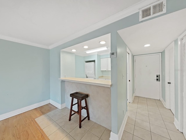 kitchen with white cabinetry, a kitchen breakfast bar, ornamental molding, kitchen peninsula, and light wood-type flooring