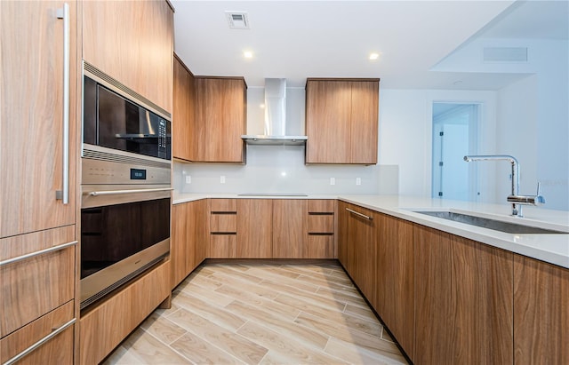 kitchen featuring wall chimney range hood, sink, kitchen peninsula, and appliances with stainless steel finishes