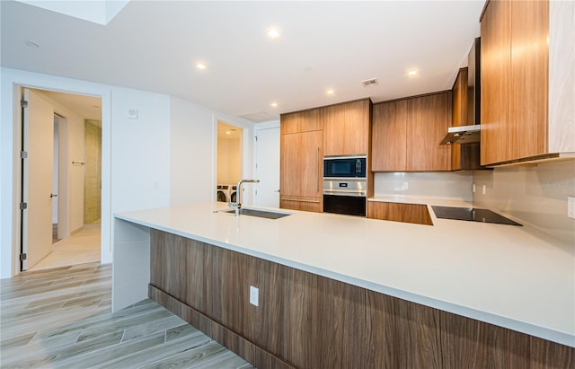 kitchen featuring wall chimney exhaust hood, sink, kitchen peninsula, light hardwood / wood-style floors, and black appliances