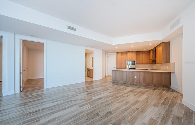 kitchen with stainless steel oven, black microwave, a raised ceiling, kitchen peninsula, and light hardwood / wood-style floors