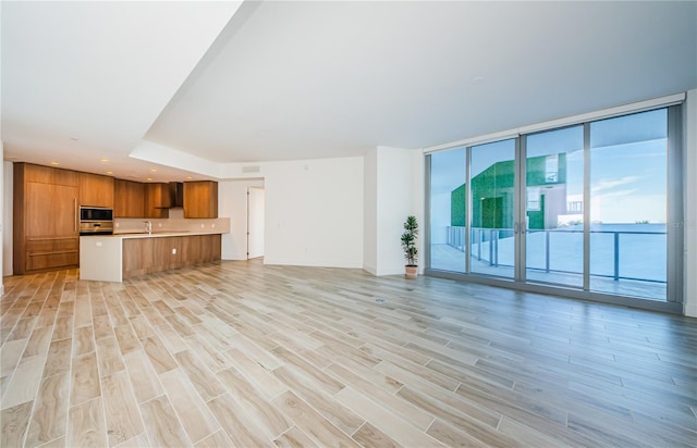 unfurnished living room featuring floor to ceiling windows, a water view, sink, and light hardwood / wood-style floors