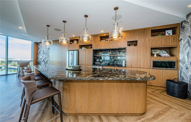 kitchen with hanging light fixtures, dark stone countertops, stainless steel refrigerator, and a wall of windows