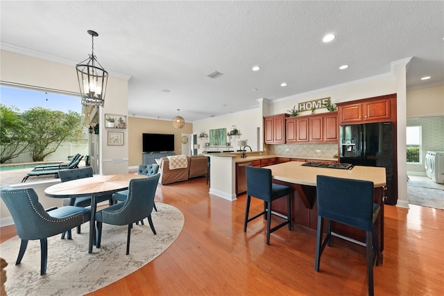 dining area with sink, crown molding, an inviting chandelier, a textured ceiling, and light wood-type flooring