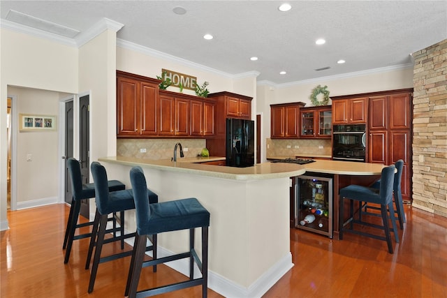 kitchen with wine cooler, hardwood / wood-style floors, a breakfast bar area, and black appliances