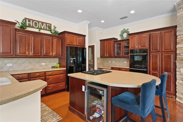 kitchen with hardwood / wood-style floors, beverage cooler, a kitchen breakfast bar, ornamental molding, and black appliances