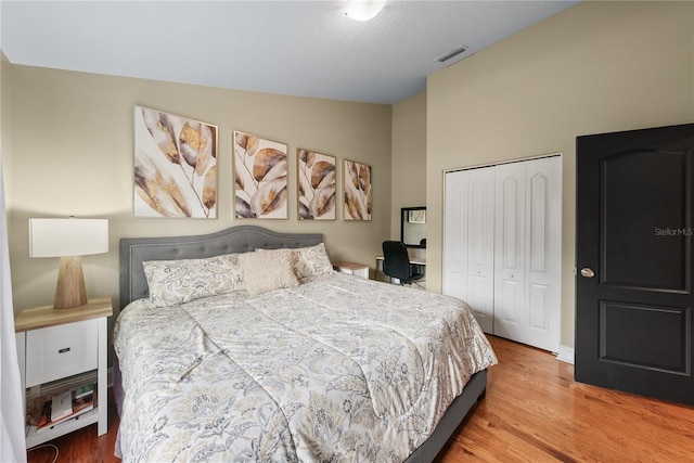 bedroom with wood-type flooring, vaulted ceiling, and a closet