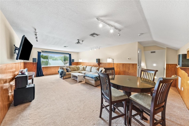 carpeted dining room with vaulted ceiling, track lighting, a textured ceiling, and wood walls