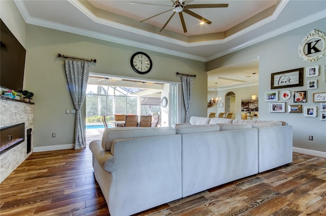 living room with a sunroom, a tray ceiling, a ceiling fan, and a stone fireplace