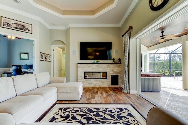 living area with a tiled fireplace, a sunroom, wood finished floors, a tray ceiling, and crown molding