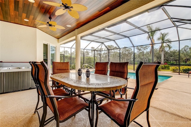 view of patio featuring a ceiling fan, outdoor dining area, glass enclosure, and a hot tub