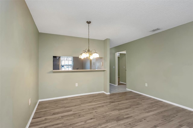 unfurnished room featuring an inviting chandelier, wood-type flooring, and a textured ceiling