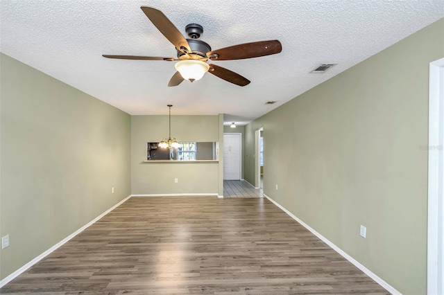 empty room with wood-type flooring, ceiling fan with notable chandelier, and a textured ceiling