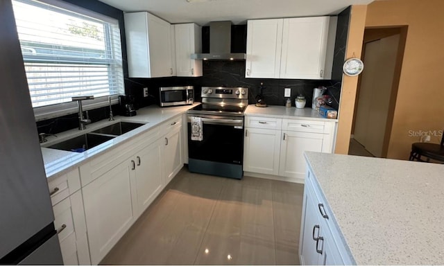 kitchen featuring appliances with stainless steel finishes, tasteful backsplash, white cabinetry, sink, and wall chimney exhaust hood