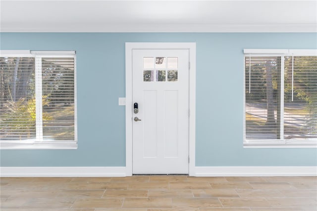 foyer entrance with light wood-type flooring, baseboards, and crown molding