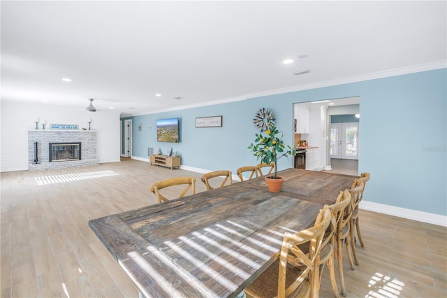 dining space featuring recessed lighting, light wood-style floors, baseboards, ornamental molding, and a brick fireplace