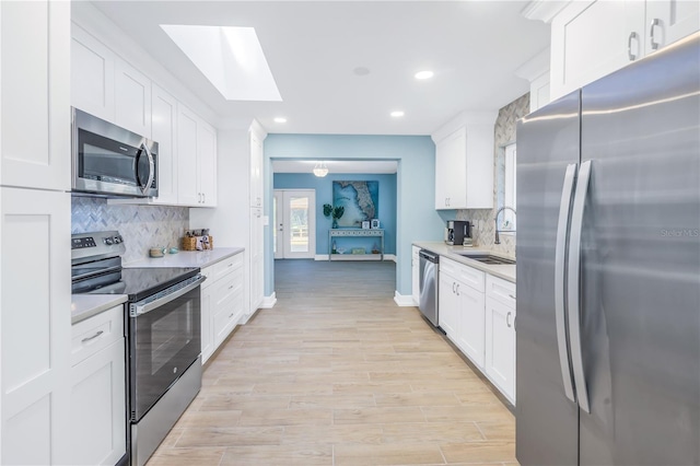 kitchen with light wood finished floors, white cabinets, appliances with stainless steel finishes, light countertops, and a sink