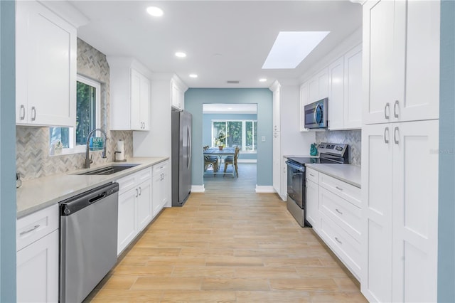 kitchen with white cabinets, stainless steel appliances, a sink, and light countertops