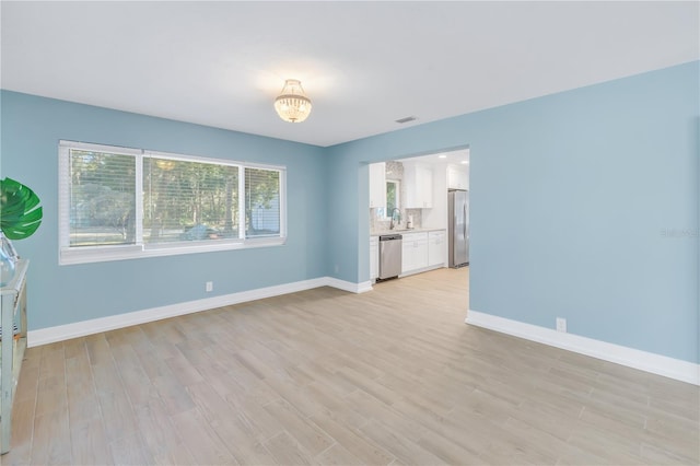 spare room with light wood-style floors, visible vents, a sink, and baseboards