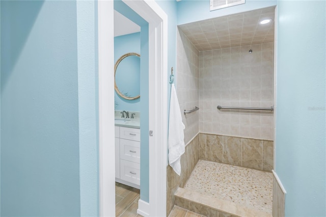 full bathroom featuring visible vents, tiled shower, and vanity