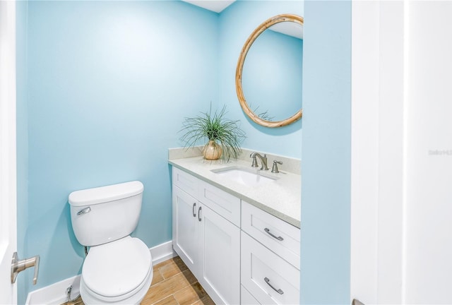 half bath featuring wood finish floors, baseboards, vanity, and toilet