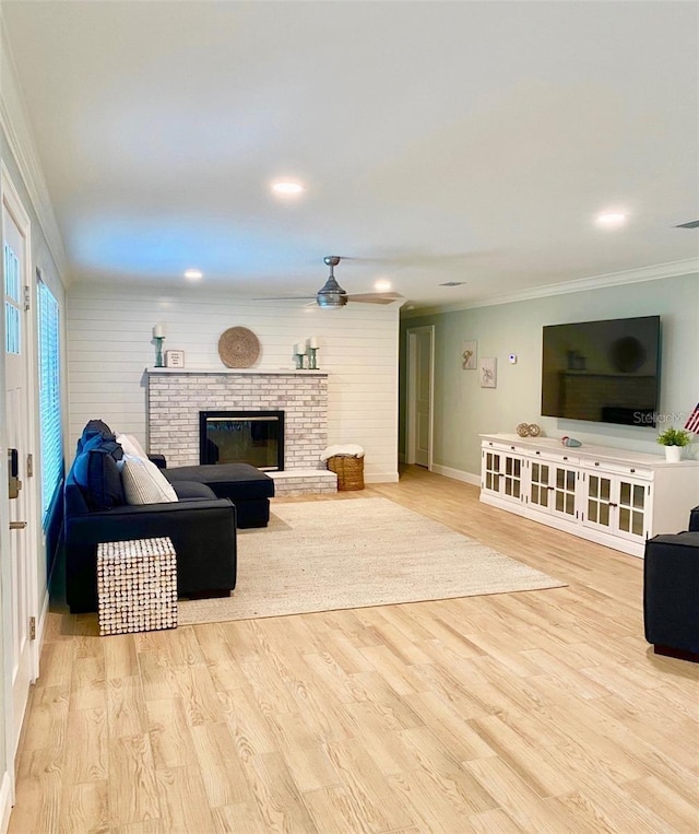 living room with wood finished floors, a ceiling fan, crown molding, baseboards, and a brick fireplace