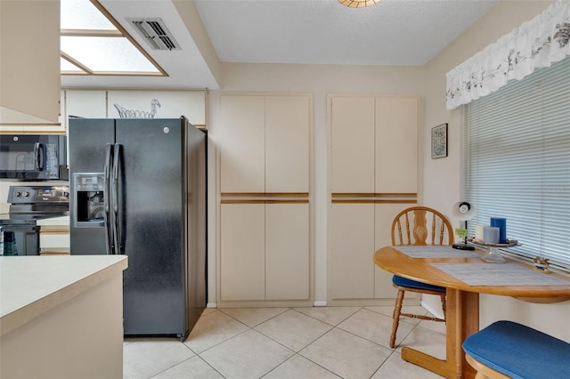 kitchen with black appliances, light tile patterned flooring, light countertops, and cream cabinetry