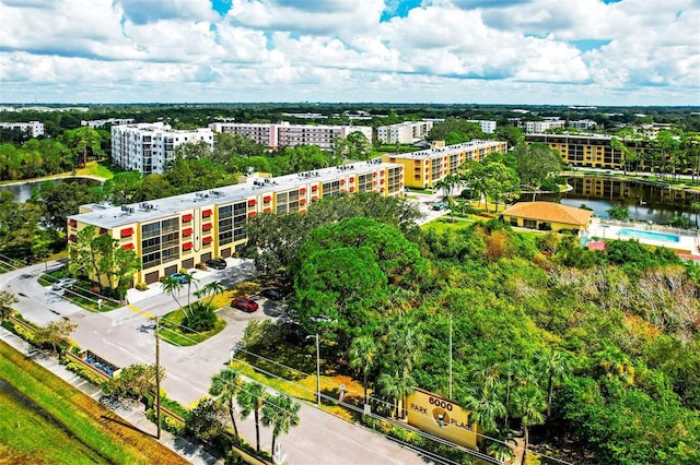drone / aerial view of apartment complex, a tree filled landscape, and a large body of water