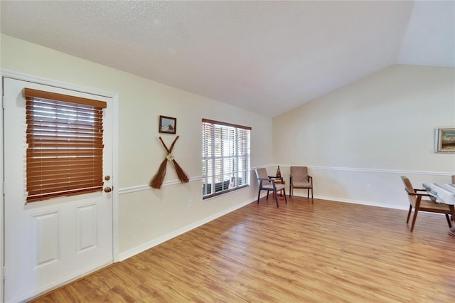 living area featuring lofted ceiling, a textured ceiling, and light hardwood / wood-style floors