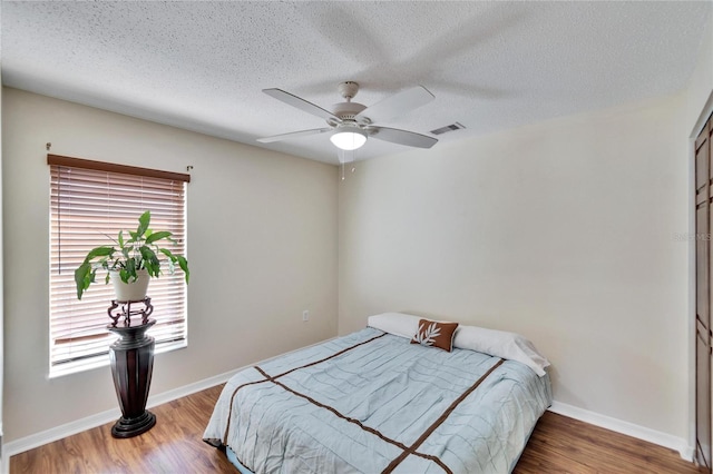 bedroom featuring ceiling fan, hardwood / wood-style floors, and a textured ceiling