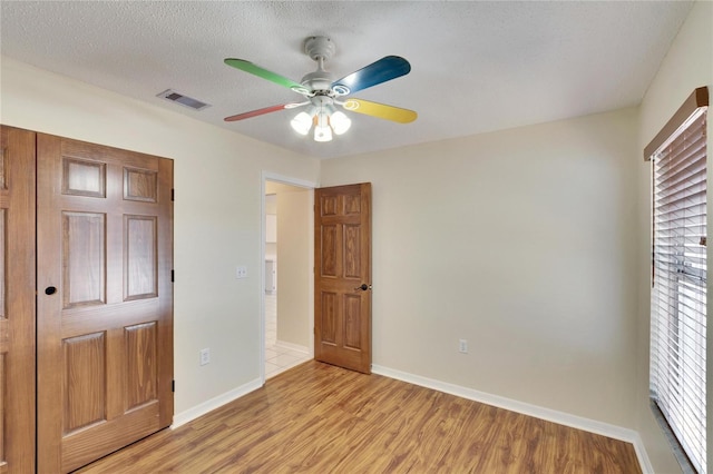 unfurnished bedroom featuring ceiling fan, a textured ceiling, and light wood-type flooring