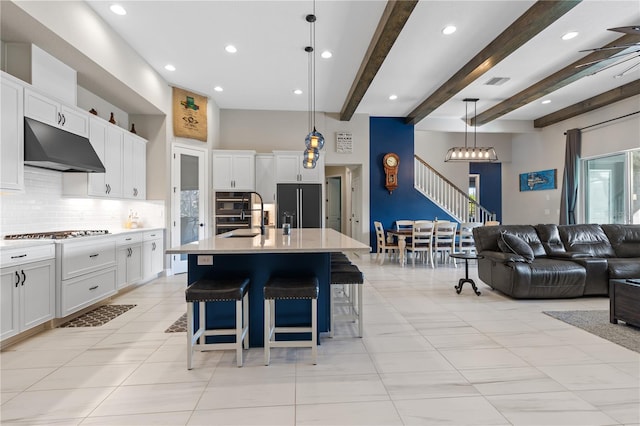 kitchen featuring built in fridge, decorative light fixtures, white cabinetry, a kitchen island with sink, and beam ceiling