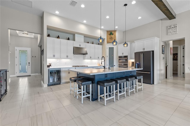 kitchen featuring a high ceiling, wine cooler, high quality fridge, a center island with sink, and decorative light fixtures