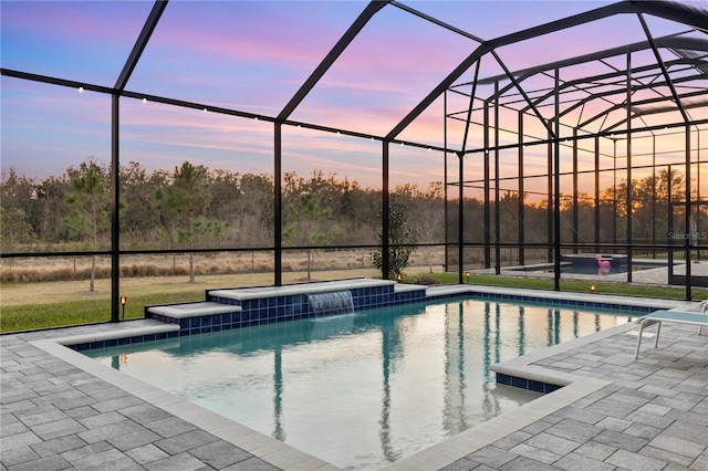 pool at dusk with pool water feature, glass enclosure, and a patio area