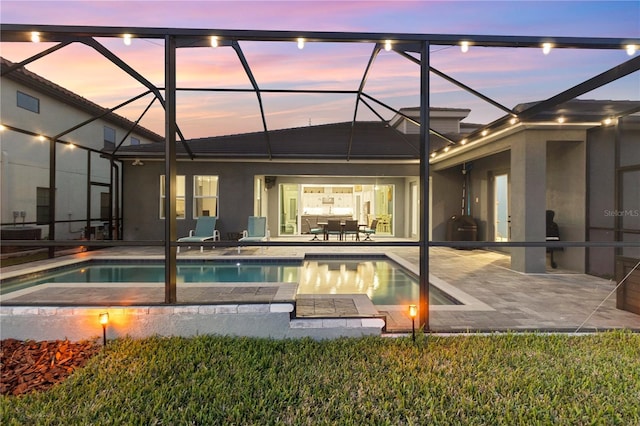 back house at dusk featuring a patio area and glass enclosure