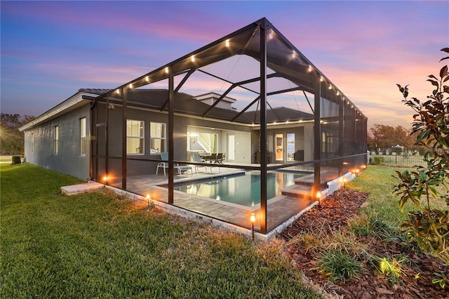 back house at dusk featuring a lanai, a patio, and a lawn