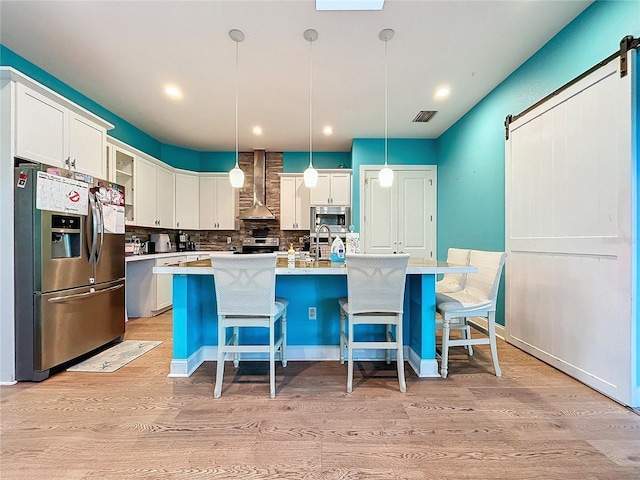 13653 Heritage Way, Sarasota, FL 34240 - kitchen with decorative light fixtures, a center island with sink, stainless steel appliances, a barn door, and wall chimney range hood