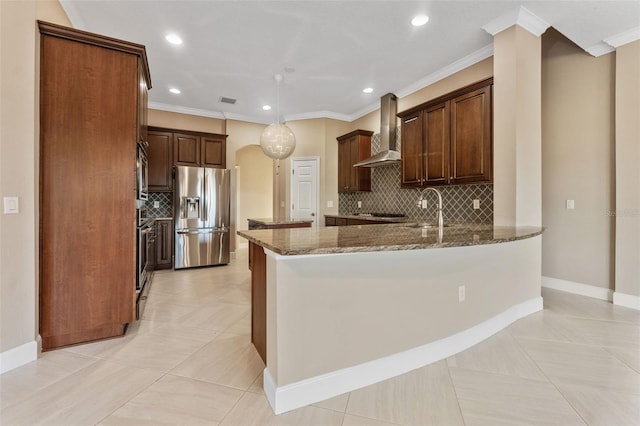 kitchen featuring sink, appliances with stainless steel finishes, kitchen peninsula, dark stone counters, and wall chimney range hood