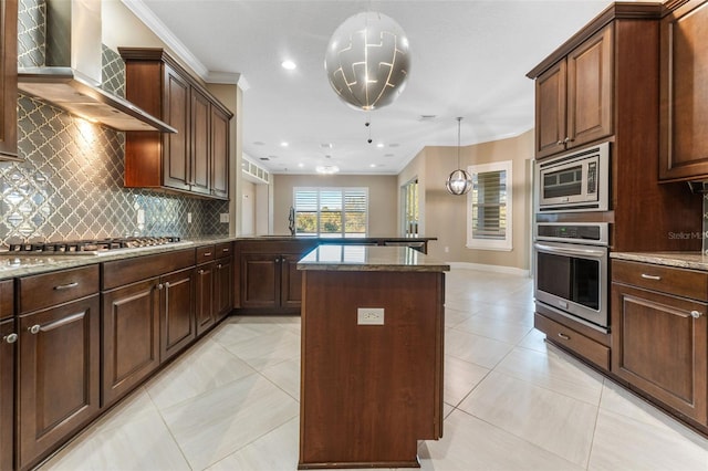 kitchen with light stone counters, hanging light fixtures, appliances with stainless steel finishes, a kitchen island, and wall chimney range hood