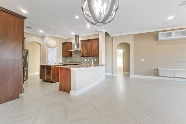 kitchen with wall chimney exhaust hood, crown molding, stainless steel fridge, light stone countertops, and backsplash