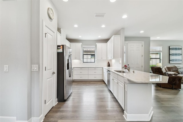 kitchen with light wood finished floors, open floor plan, appliances with stainless steel finishes, a peninsula, and a sink