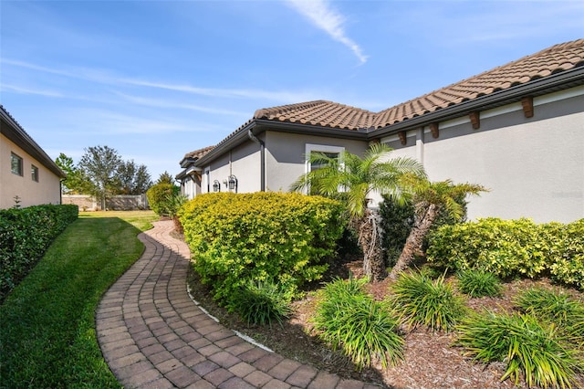 view of side of property with stucco siding, a tile roof, a yard, and fence