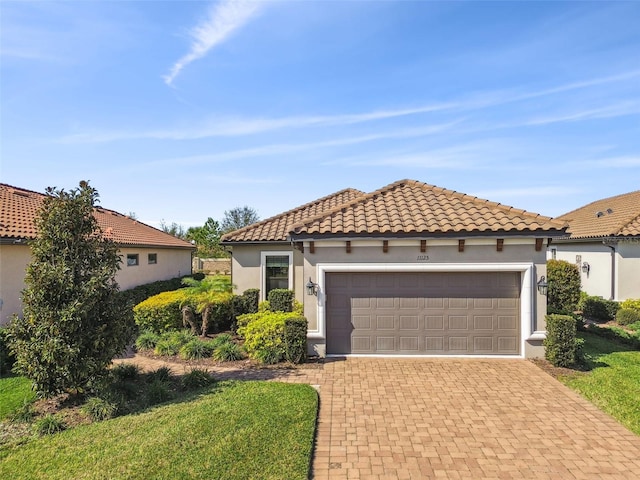 mediterranean / spanish-style house featuring a garage, stucco siding, a tiled roof, and decorative driveway