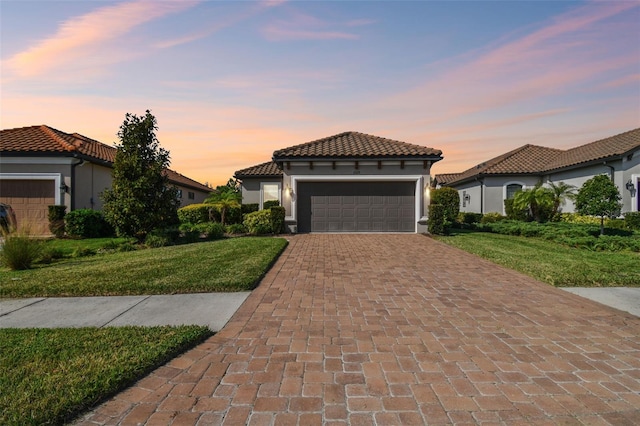 mediterranean / spanish-style house featuring a tiled roof, stucco siding, decorative driveway, a front lawn, and an attached garage
