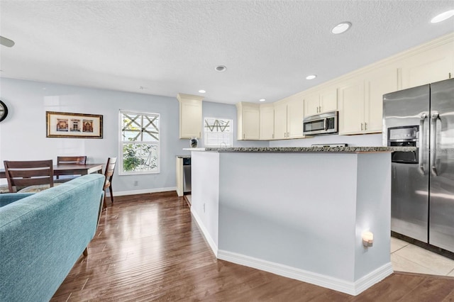 kitchen featuring hardwood / wood-style flooring, stainless steel appliances, cream cabinets, and a textured ceiling