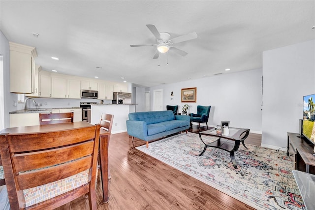 living room featuring ceiling fan, sink, and light hardwood / wood-style floors