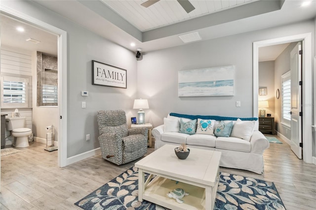 living room featuring a raised ceiling, wood ceiling, ceiling fan, and light hardwood / wood-style flooring